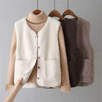 Three sherpa fleece puffer vests in white, dark brown and taupe hanging on wooden hangers with a hand showing the soft suede lining