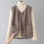 Grey-taupe sherpa fleece vest layered over a cream turtleneck jumper, hand peeling open the front to show the inner lining