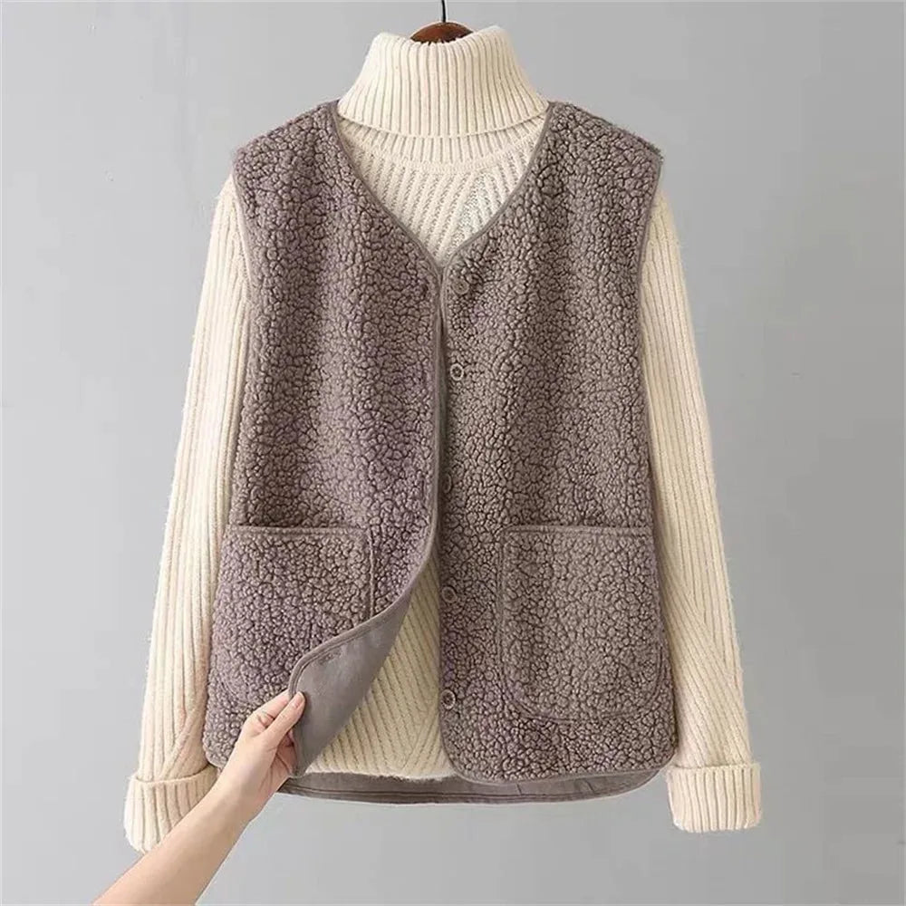 Grey-taupe sherpa fleece vest layered over a cream turtleneck jumper, hand peeling open the front to show the inner lining