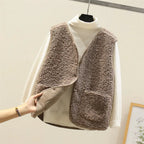 Taupe-brown sherpa fleece vest over a cream jumper, hand lifting the hem to reveal the smooth suede-like inner lining