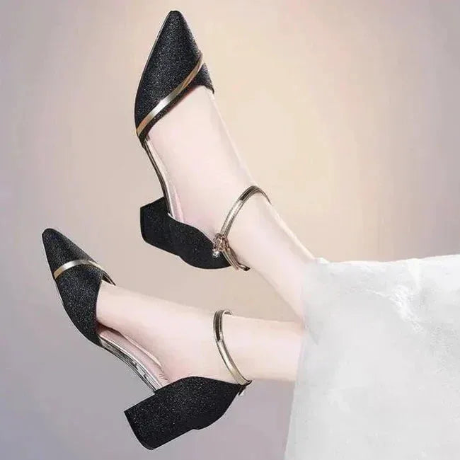 Model wearing black glitter block heel sandals with gold ankle strap, legs crossed against a draped skirt