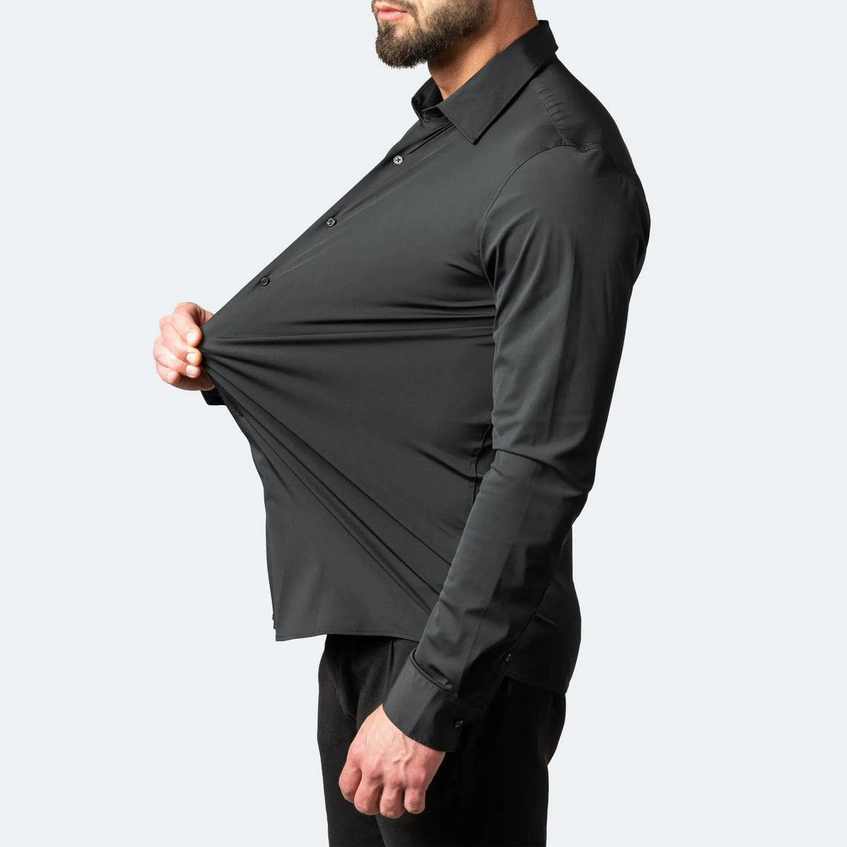 Side view of a man pulling the black shirt fabric at the chest to show its stretch across the torso
