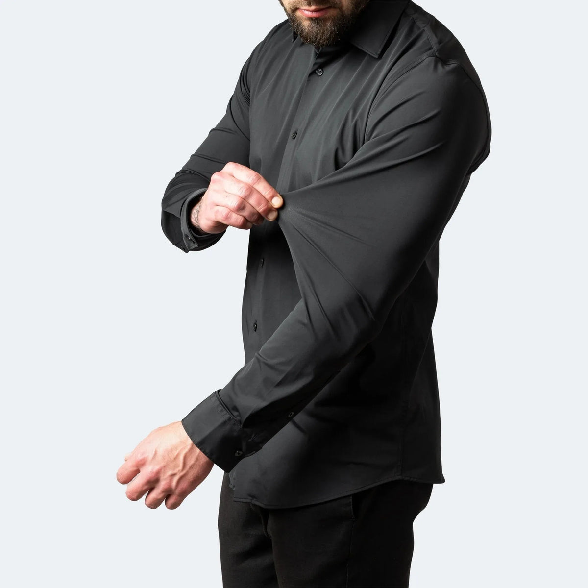 Close-up of a man stretching the sleeve fabric of a black slim-fit shirt to show flexible movement