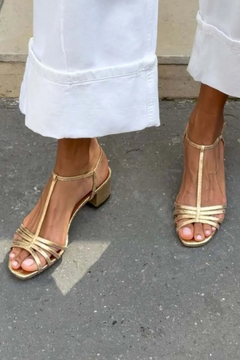 Front view of gold metallic T-strap sandals with strappy toe detail on model wearing white trousers