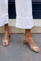 Side angle of gold strappy block heel sandals showing low stable heel against pavement