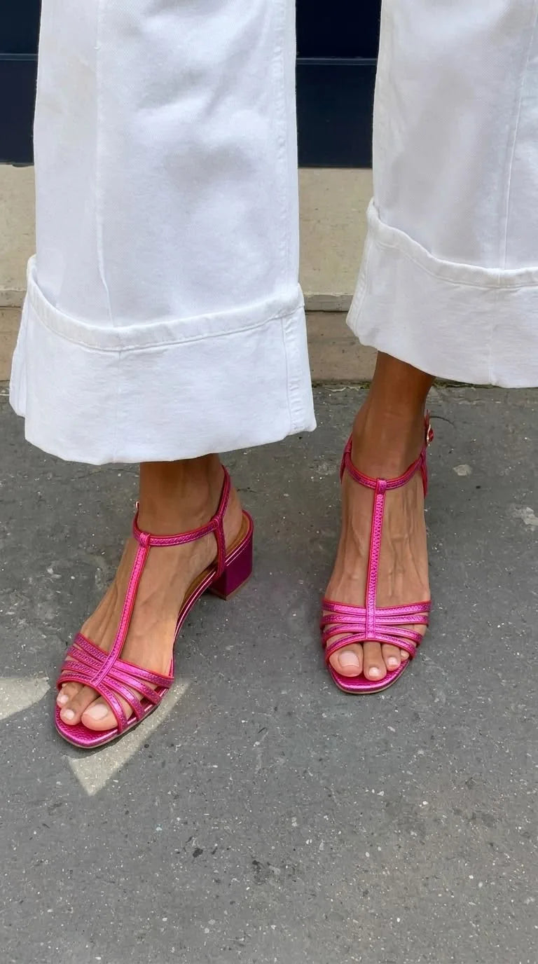 Pink metallic T-bar sandals with strappy front and low block heel, paired with white cropped pants