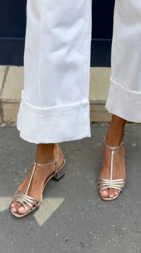 Pale gold shimmer sandals with crisscross front straps and T-bar detail on bare feet