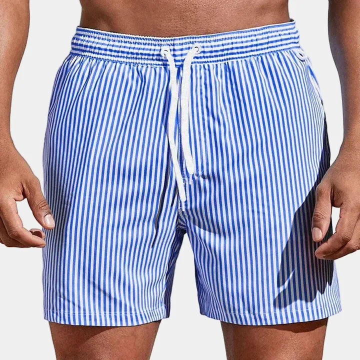 Front view of man wearing blue and white vertical striped boardshorts with white drawstring waist.