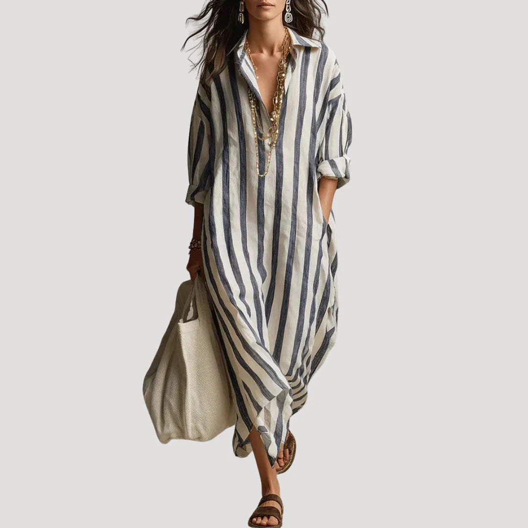 Front view of a woman in a flowing blue and white striped linen shirt dress with a layered gold necklace and tote bag
