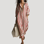 Front view of the long shirt dress in a red and white striped linen blend, worn with sandals and a woven tote