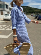 Side view of woman in blue and white striped midi shirt dress with rolled 3/4 sleeves, carrying a woven straw tote