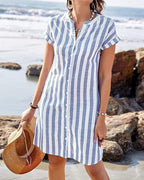 Close view of the button placket and V-neckline on the striped midi dress, paired with a woven straw bag