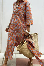 Woman walking in orange and blue geometric print midi shirt dress with rolled sleeves and straw tote bag