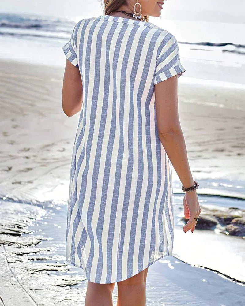 Back view of the striped midi dress showing the relaxed fit and curved hemline on the sand