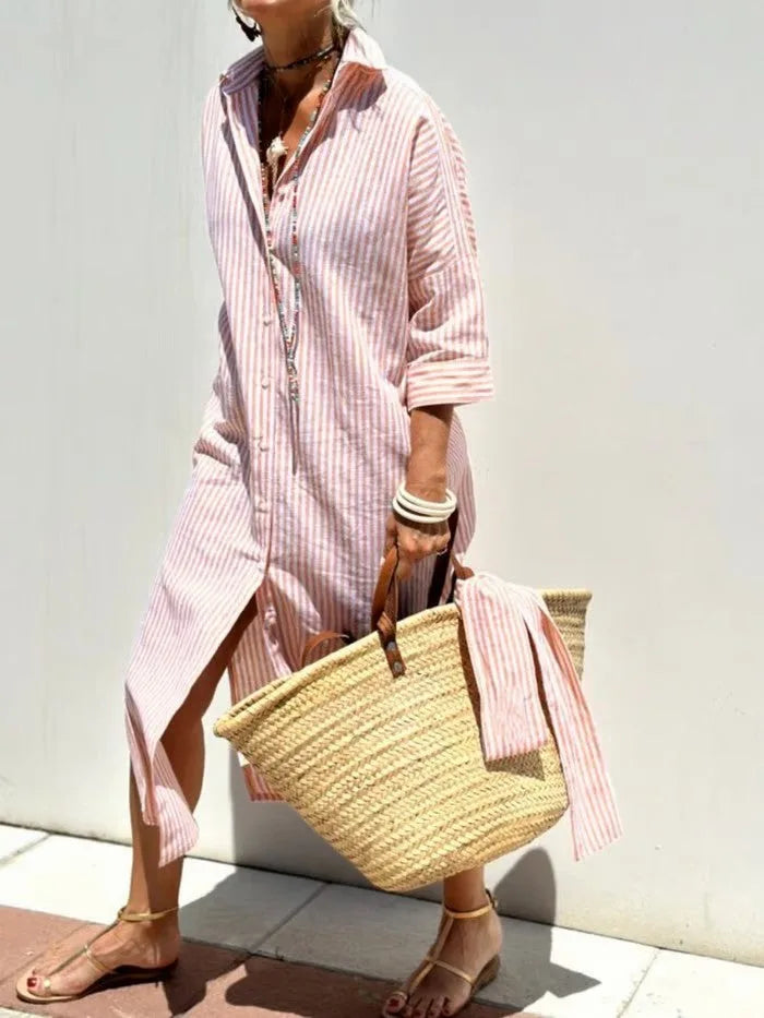 Front view of pink and white striped button-front midi dress with side slit and straw beach bag