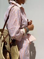 Close-up of coral and white striped linen-blend fabric with rolled sleeve cuff and tied waist detail