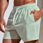 Close-up side view of green and white striped boardshorts with hand tucked into side pocket