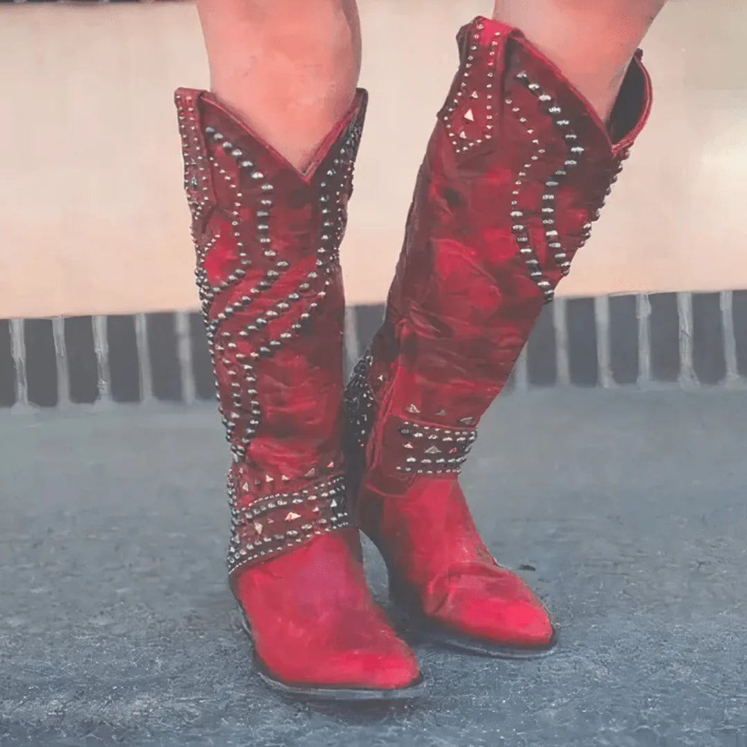 Front view of red studded knee-high western boots with silver stud detailing and pointed toes, worn with jeans tucked in