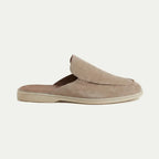 Side profile of a beige suede slip-on mule with closed toe, open heel and visible top stitching on a cream sole