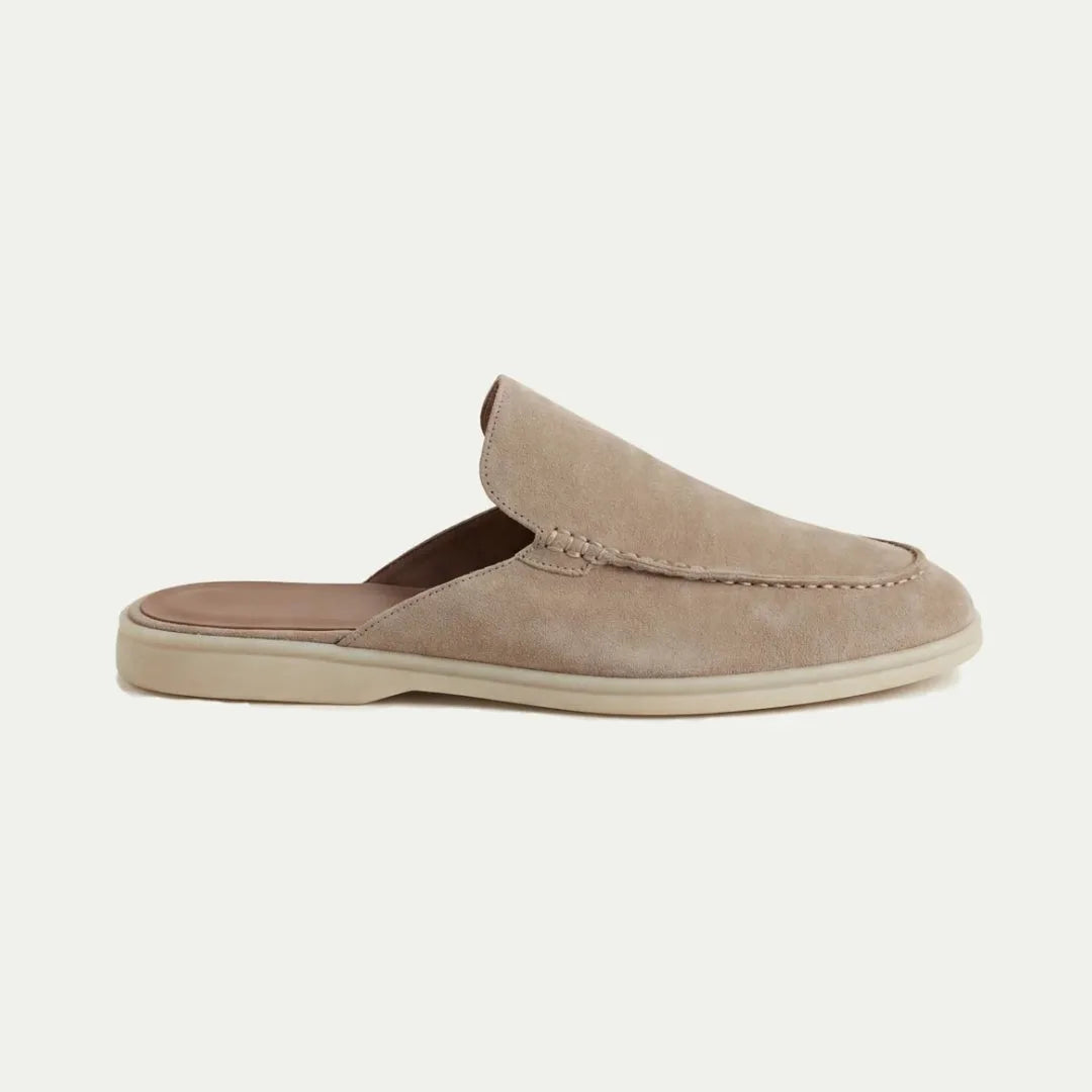 Side profile of a beige suede slip-on mule with closed toe, open heel and visible top stitching on a cream sole
