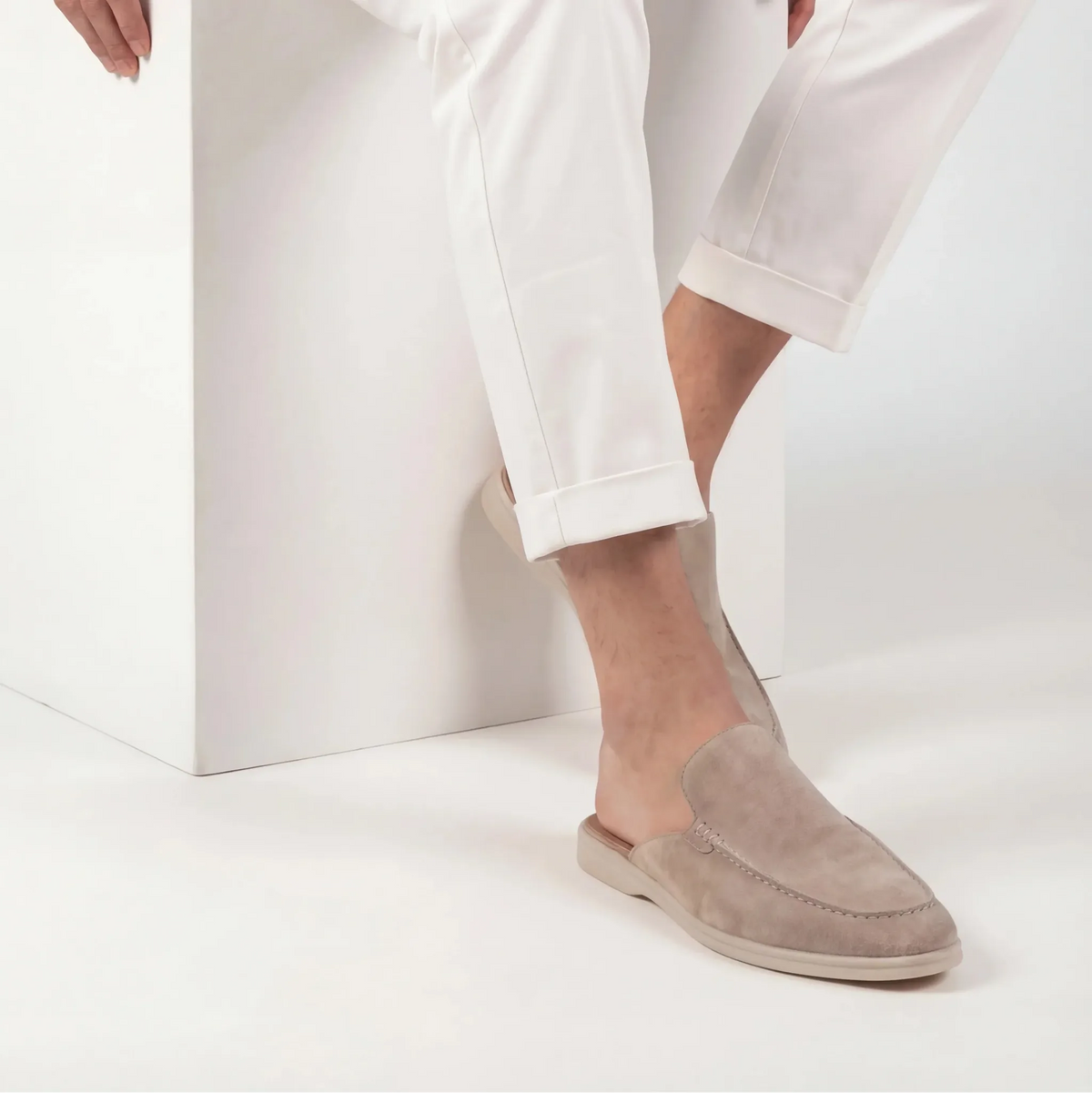 Man wearing a taupe suede mule with white cuffed trousers, showing the open backless heel design in use