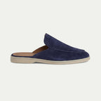 Side view of a navy suede backless loafer mule with stitched apron toe and light cream rubber sole