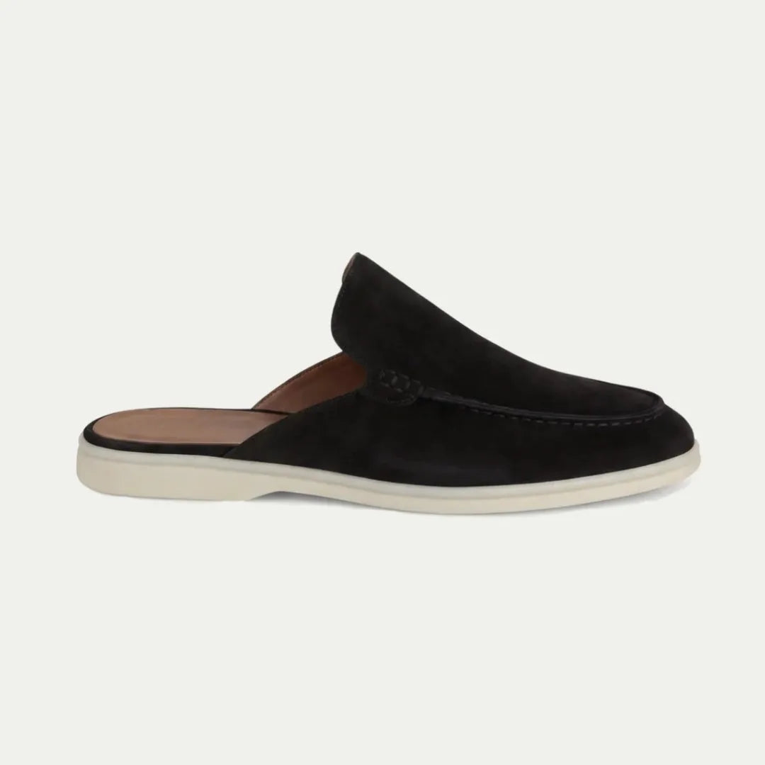 Side profile of a black suede slip-on mule with closed toe, open back and contrasting cream sole