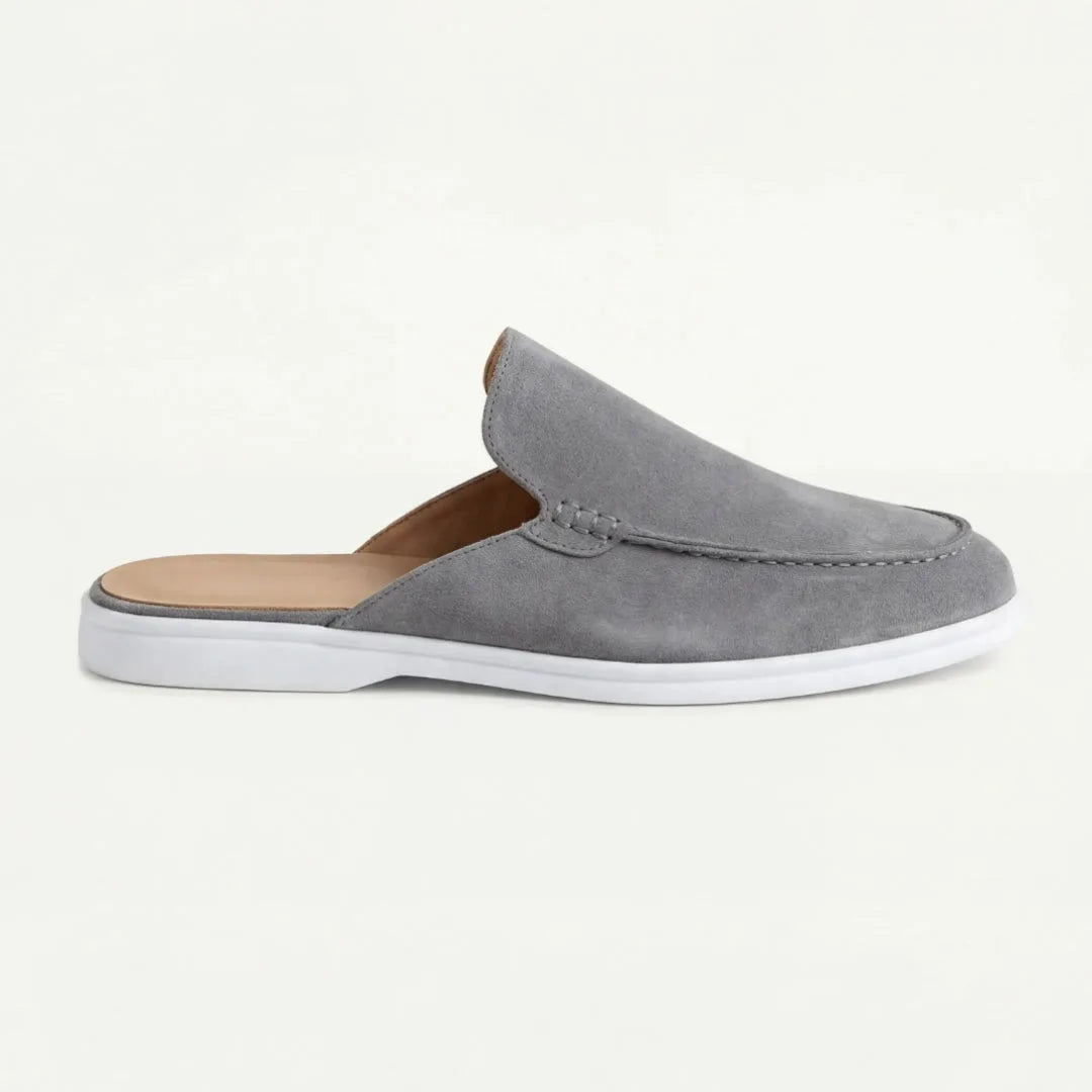 Side view of a grey suede backless mule with stitched apron front and crisp white rubber sole