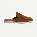 Side profile of a tan brown suede slip-on mule with open heel, stitched toe seam and cream sole
