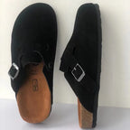 Black suede clog slippers shown side by side, highlighting the buckle hardware and cork-edged sole
