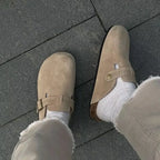 Close-up on feet wearing beige suede clogs with white socks, one shoe shown from the front and one from the side