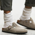 Close-up of feet in taupe suede clogs worn with slouchy knit socks and rolled-up trousers