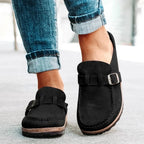 Black suede backless loafers with buckle strap and stitched sole, front angle on model wearing jeans