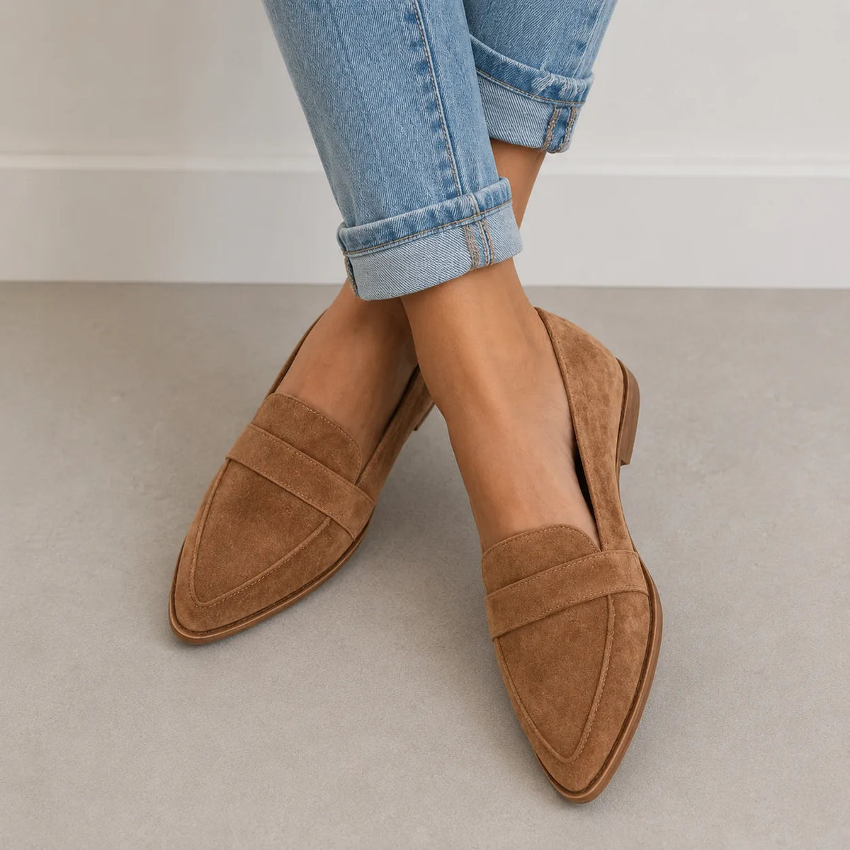 Close-up of crossed feet wearing tan suede pointed-toe loafers with a stacked block heel and penny strap detail