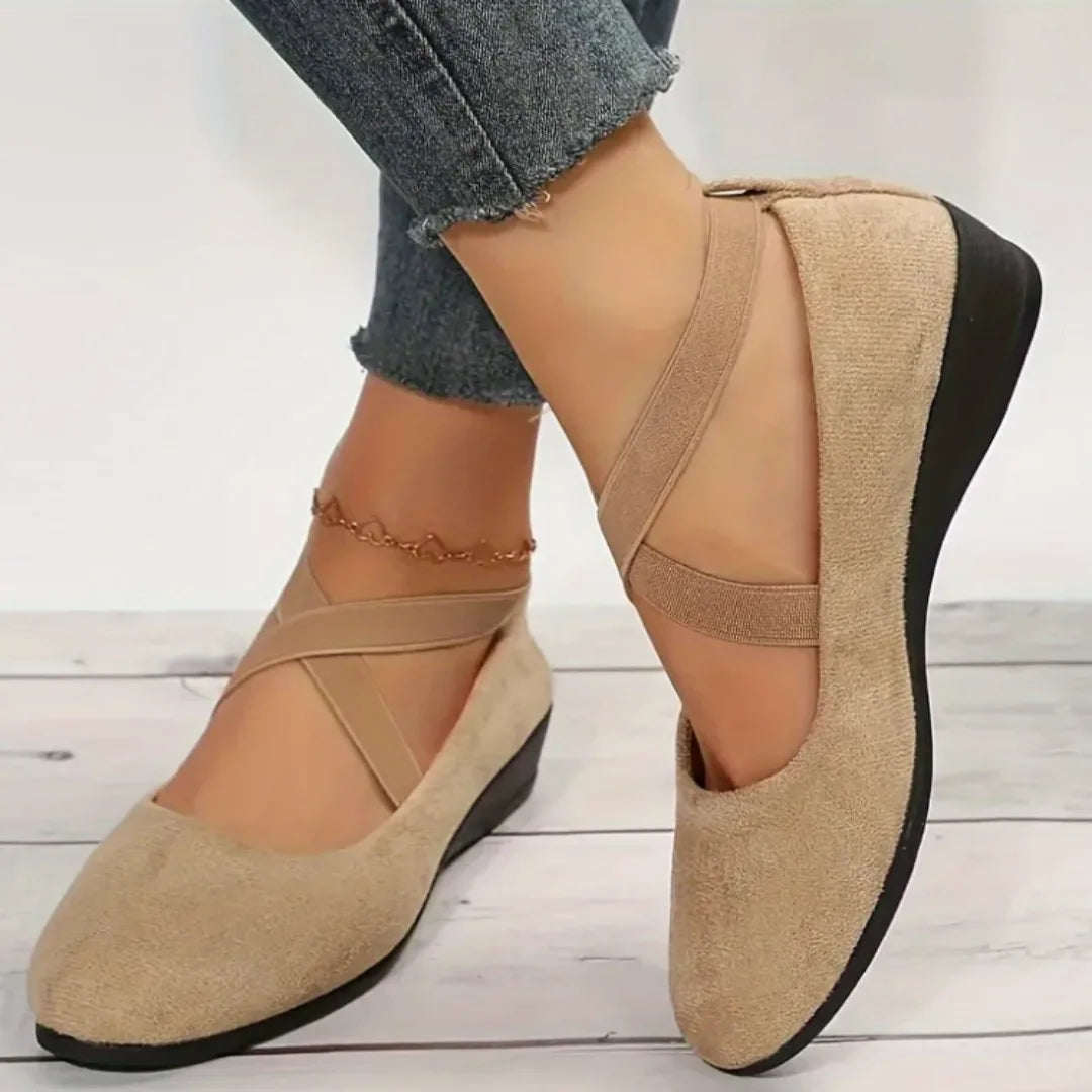 Angled view of beige suede crisscross-strap flats showing the low wedge heel and stitched footbed