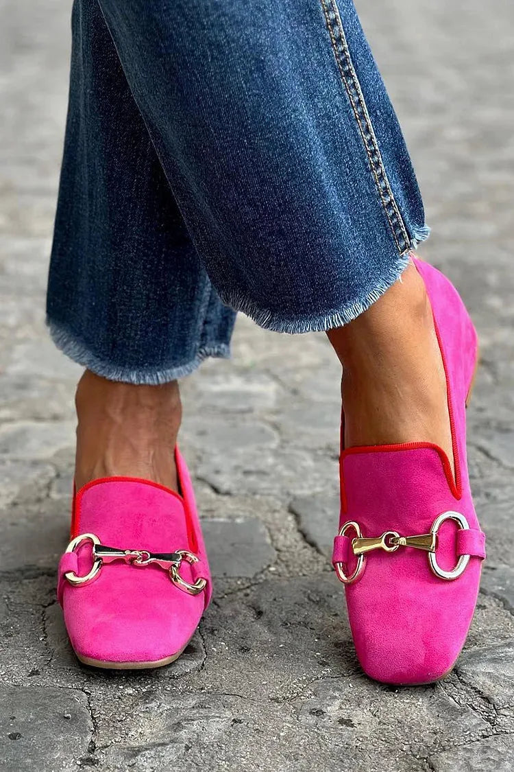 Close-up front view of magenta pink suede loafers with gold horsebit buckle and red piping, worn with cropped jeans