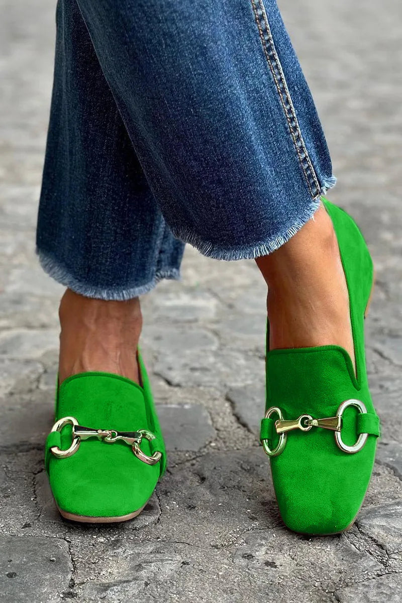 Bright green suede loafers with gold horsebit hardware, shown from the front while walking on cobblestones