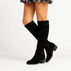 Black suede knee-high boot with ankle strap detail paired with a floral mini skirt