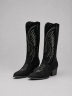 Pair of black suede knee-high cowboy boots with contrast stitching, shown angled on a plain grey background