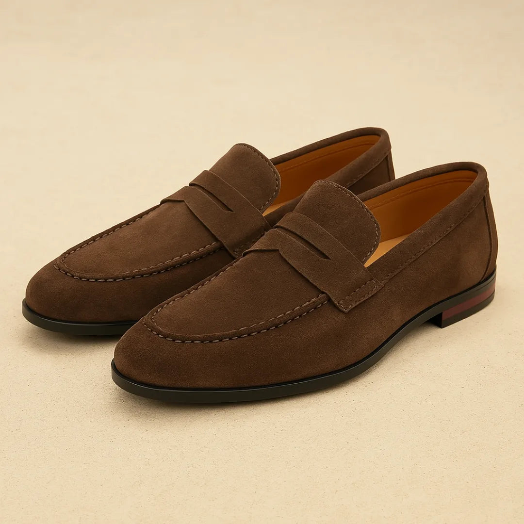 Pair of dark brown suede penny loafers shown at an angle, highlighting the apron stitching and tan leather lining