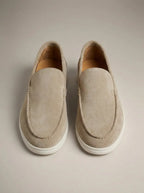 Top-down view of beige suede slip-on loafers with white outsole and tan leather lining on a neutral backdrop
