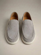 Grey suede slip-on loafers photographed from above against a plain backdrop, with white rubber sole