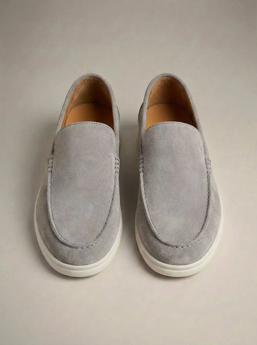 Grey suede slip-on loafers photographed from above against a plain backdrop, with white rubber sole