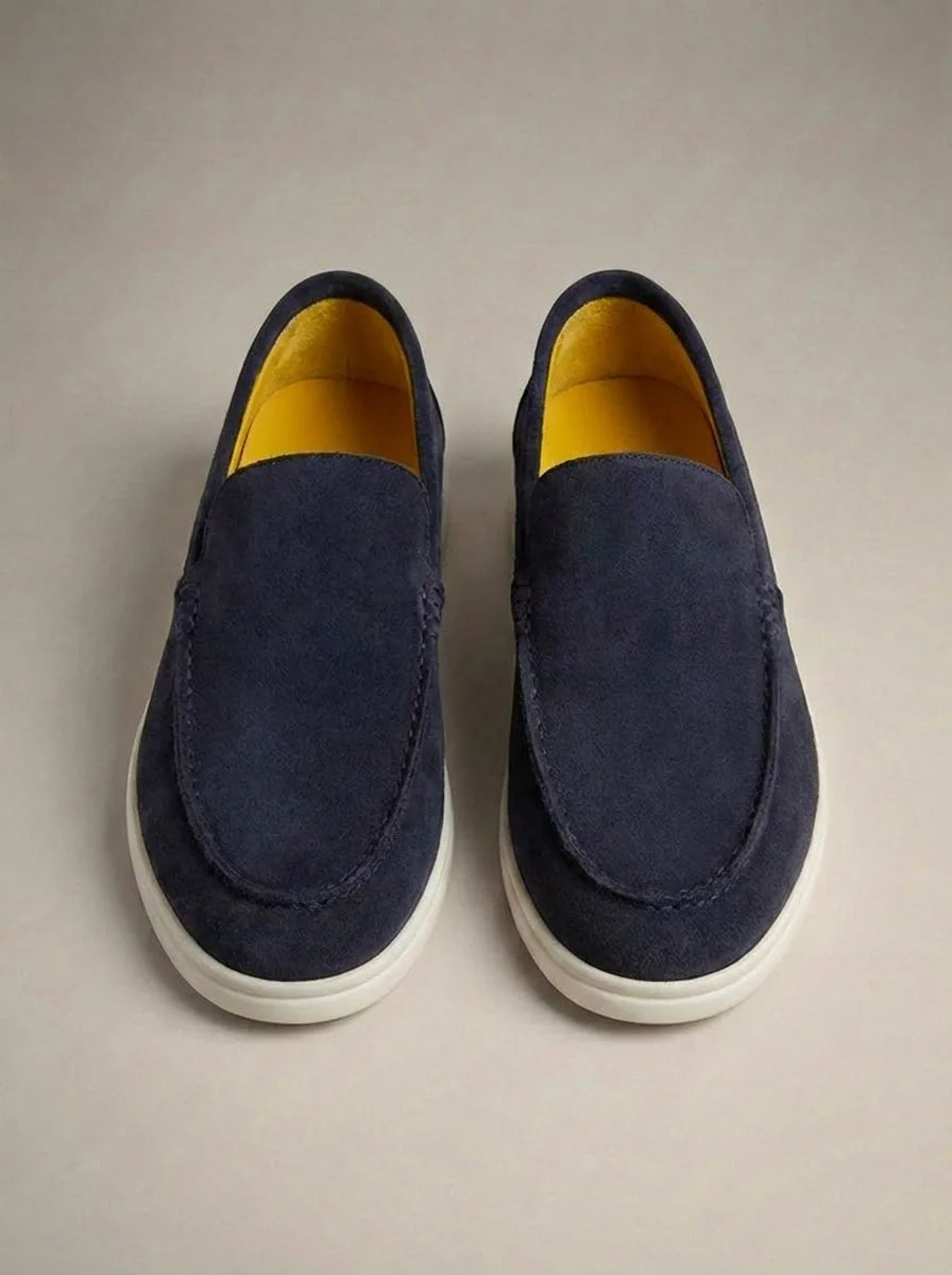 Navy suede slip-on loafers with a striking yellow leather lining, shown from directly above