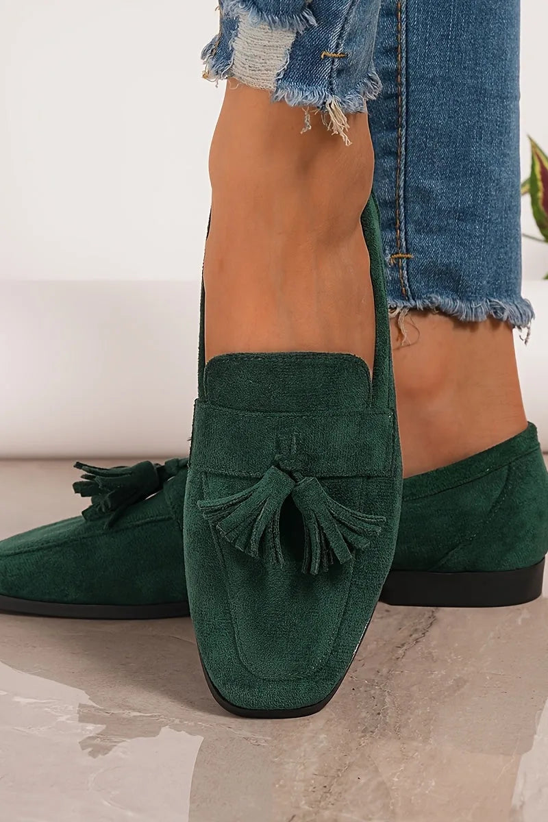 Close-up front view of the dark green tassel loafer worn with cropped frayed jeans, showing the suede texture and square toe