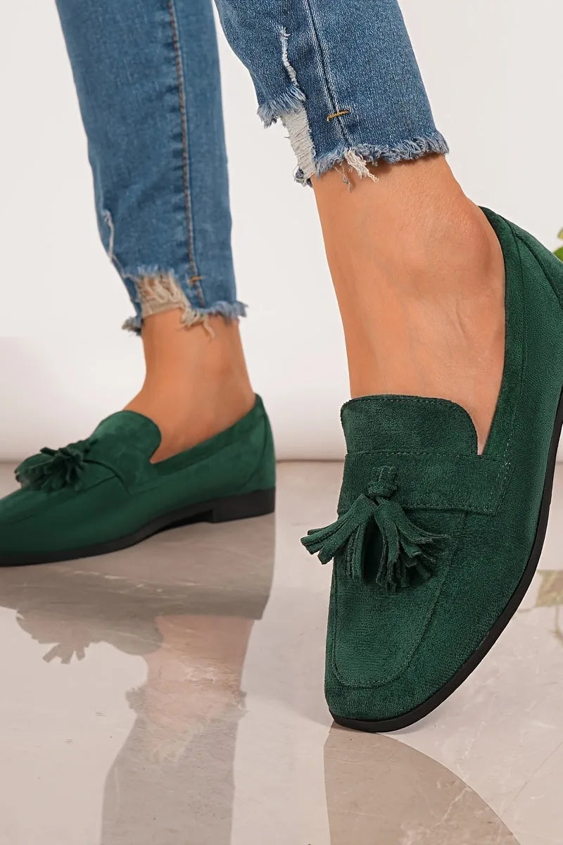Side angle of the dark green suede tassel loafer on foot, highlighting the stitched apron and flat black sole