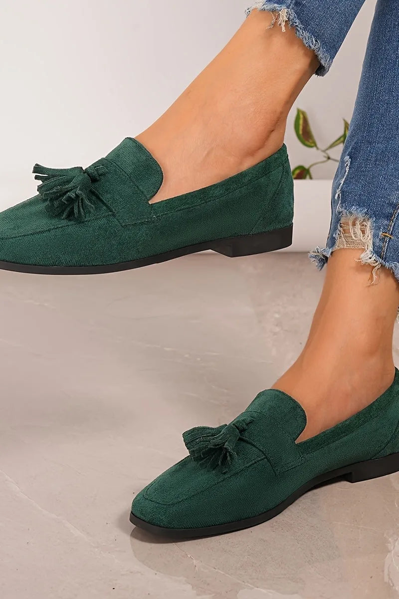 Both dark green tassel loafers shown together on feet with cuffed denim, showcasing the low heel and classic loafer shape