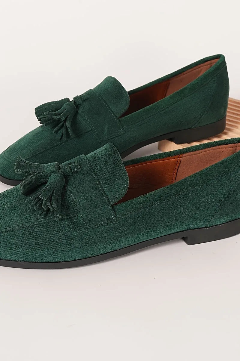 Pair of dark green tassel loafers resting on a marble floor, displaying the matching tassel detail and sleek silhouette