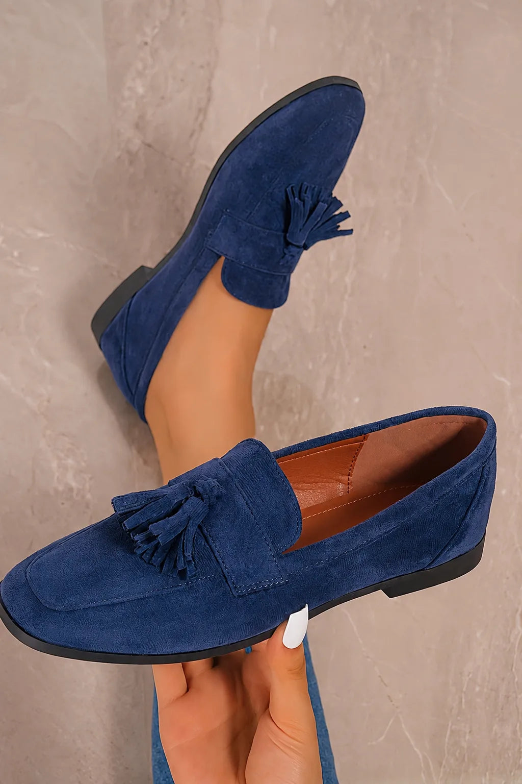 Close-up of the dark green suede loafers on a wooden stand, revealing the tan leather lining and tassel trim