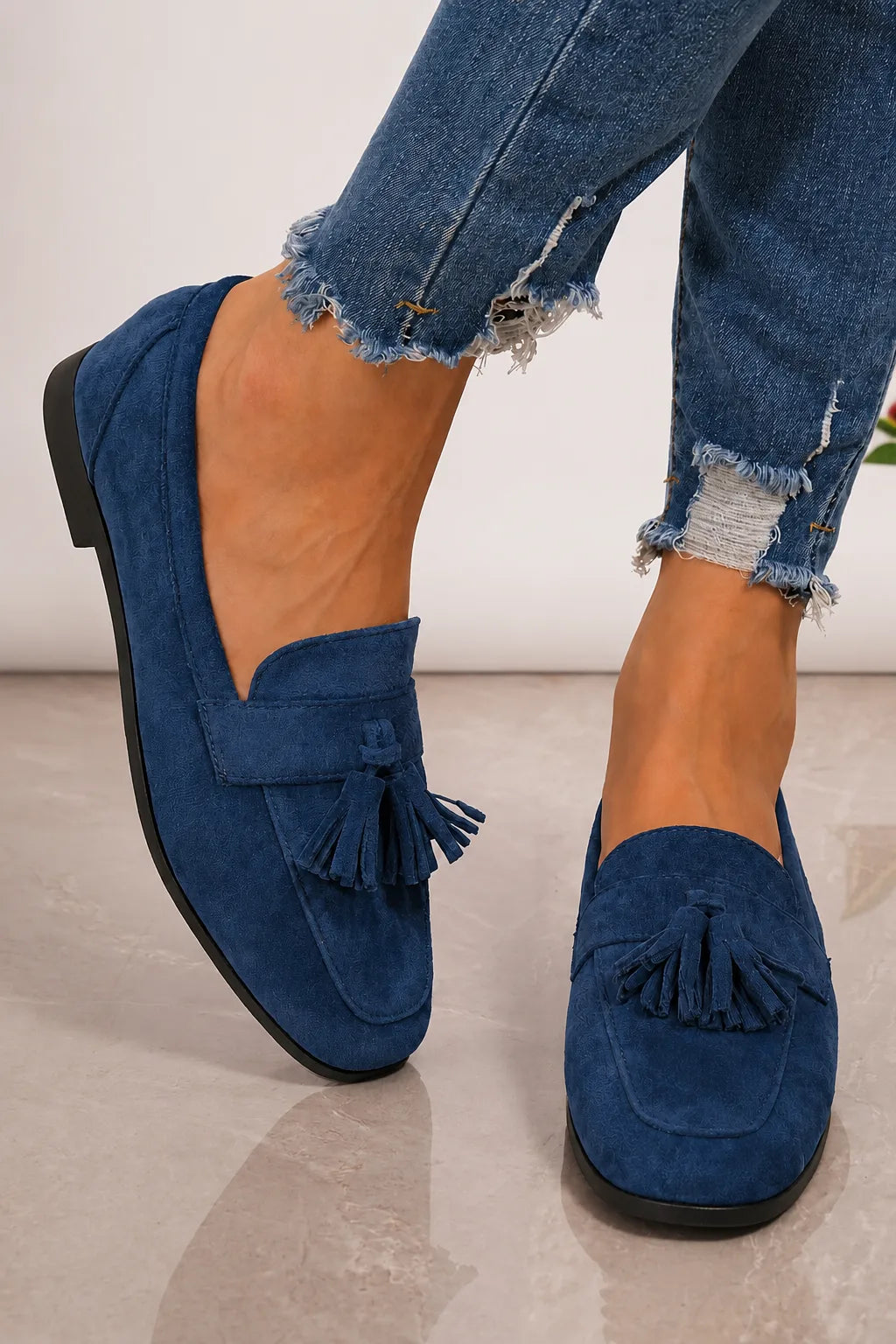 Navy blue suede tassel loafer held up by hand, showing the tan interior lining and stitched tassel detailing